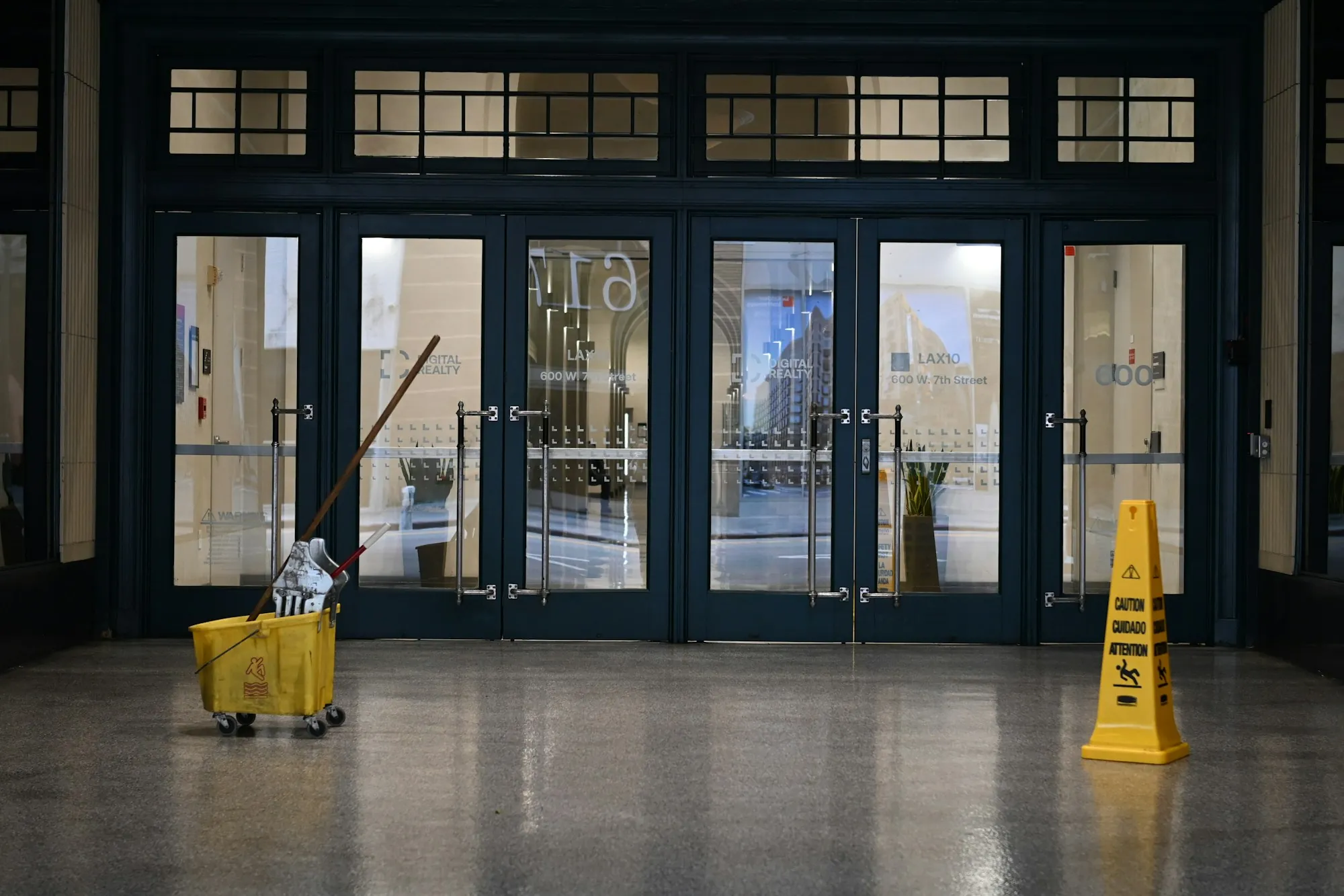 Mop bucket and wet floor sign inside a glass building entrance